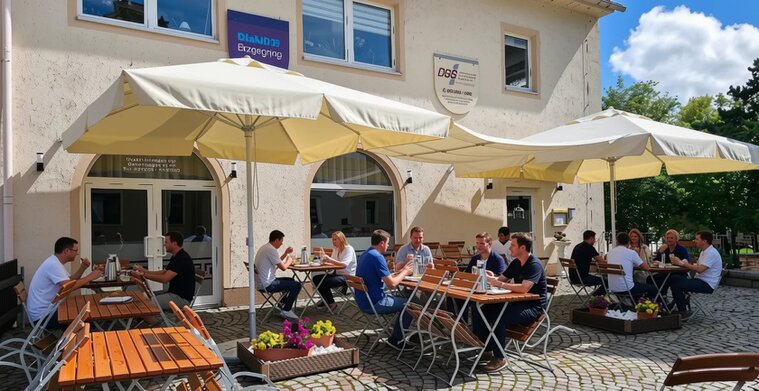 Biergarten der Taverne Nostos mit Gästen an Holztischen